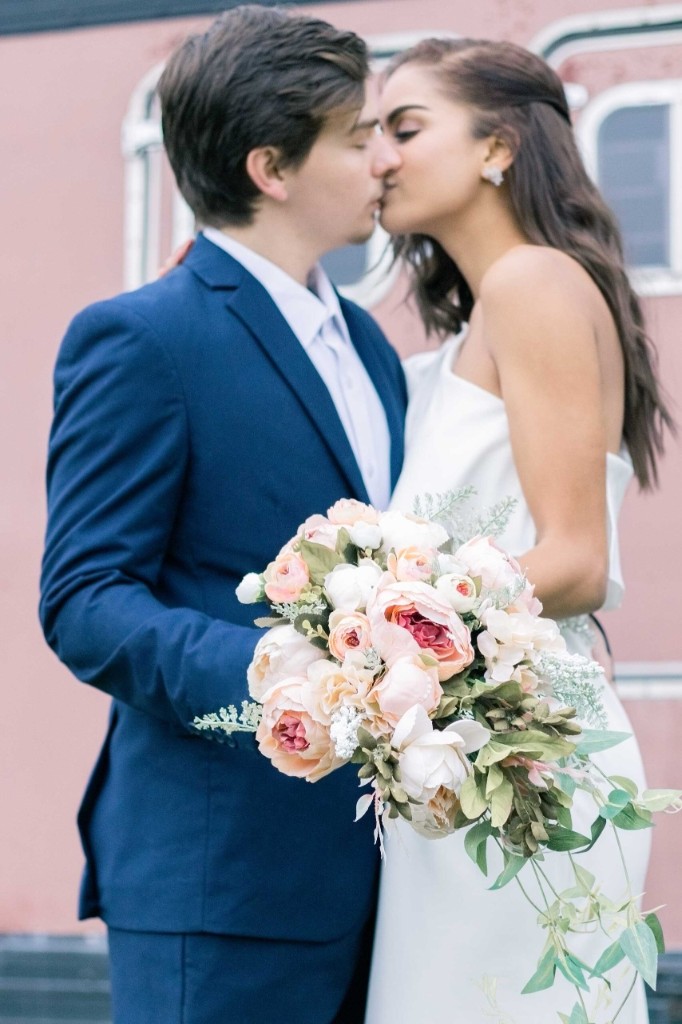 Couple kissing behind a soft pink and peach rose bouquet — Abigail Dumlao Photography & Film