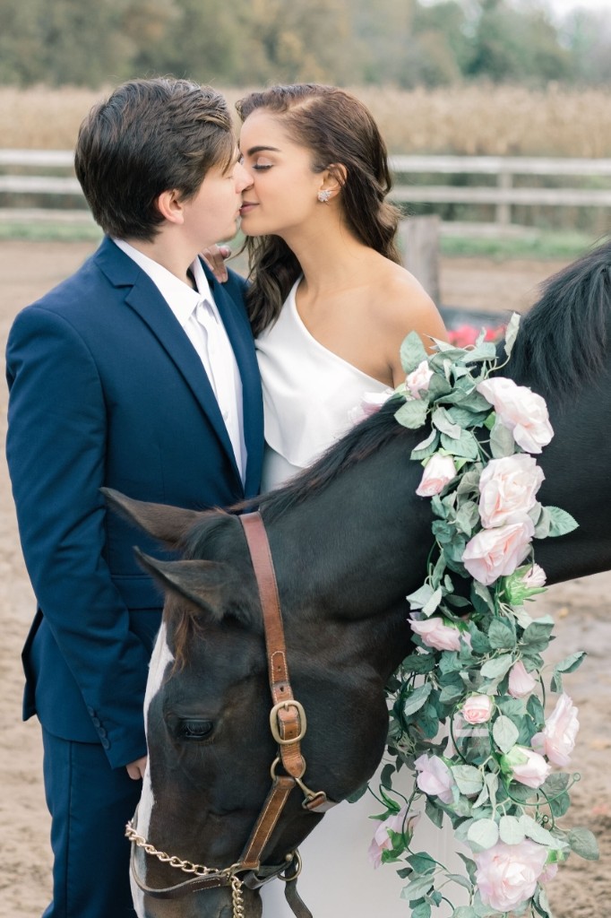 Couple kissing beside a dark horse with a pink rose garland — Abigail Dumlao Photography & Film